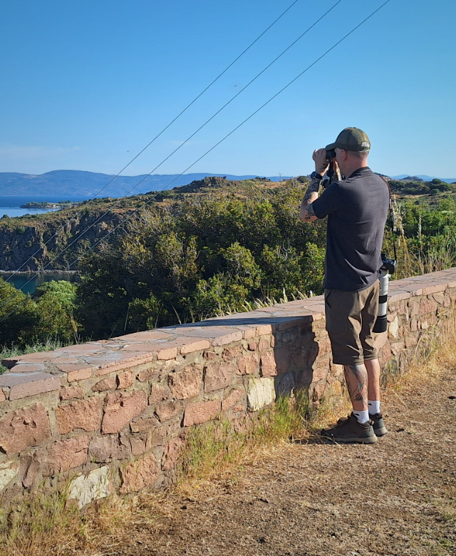 The Trip Tick founder birdwatching with binoculars over a coastal bay in Lesvos, Greece
